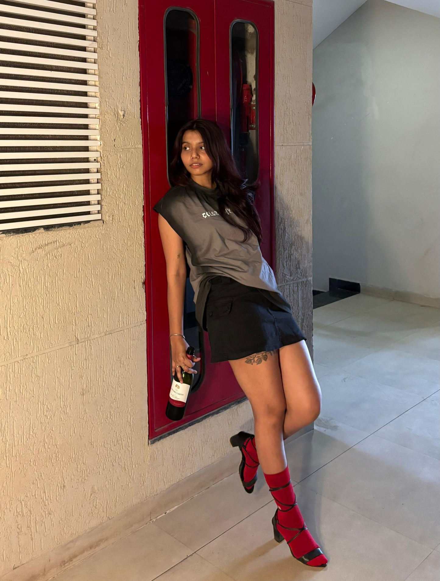 Woman posing in a hallway with a red door and light-colored walls.