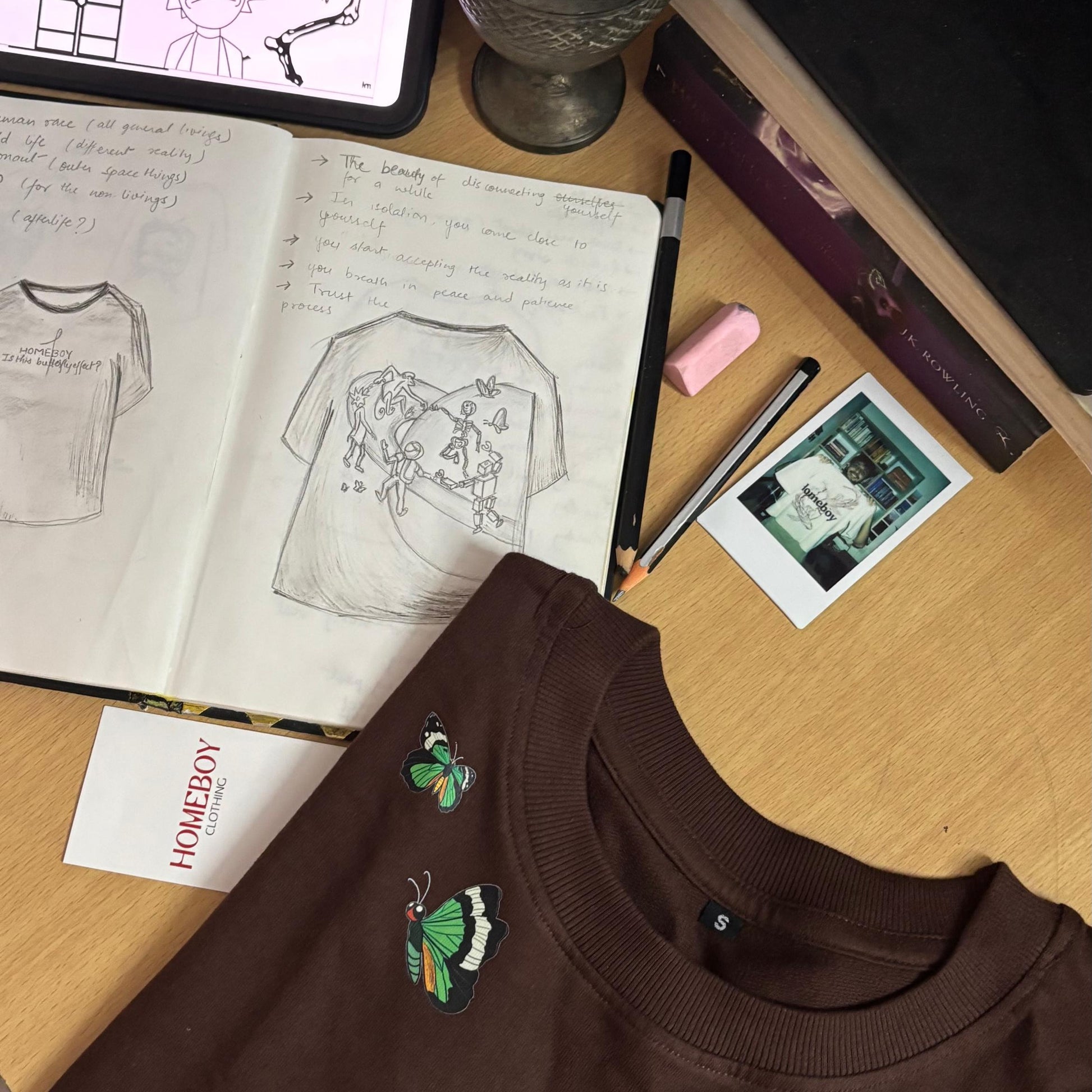 Brown t-shirt with 'HOMEBOY' text on a desk with sketches and stationery.